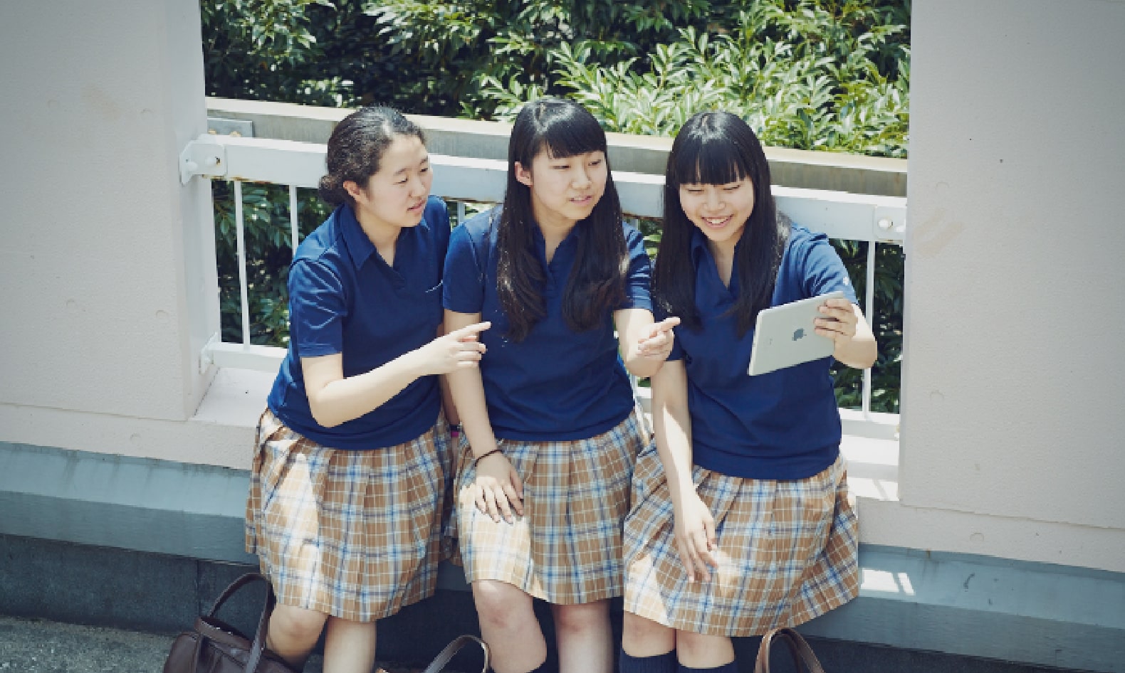 タブレットを指さしながら会話している3人の女子生徒の写真